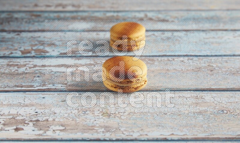 45º Shot of two Yellow Crème Brulée macarons on light blue wooden background