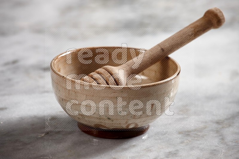 Beige Pottery bowl with wooden honey handle in it, on grey marble flooring, 15 degree angle