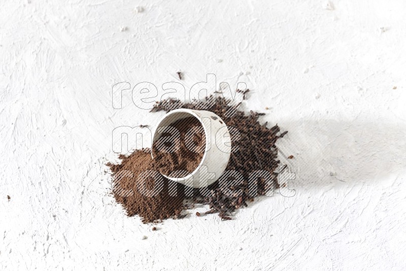 A beige ceramic bowl with cloves powder spilled out of it on a textured white flooring