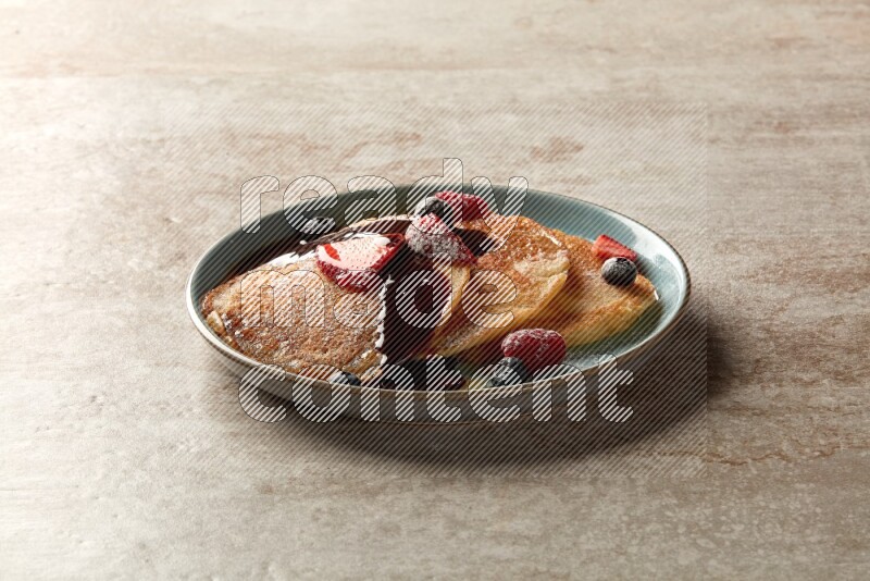 Three stacked mixed berries pancakes in a blue plate on beige background