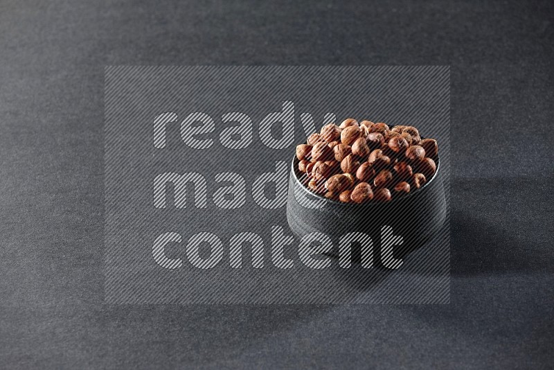 A black pottery bowl full of peeled hazelnuts on a black background in different angles