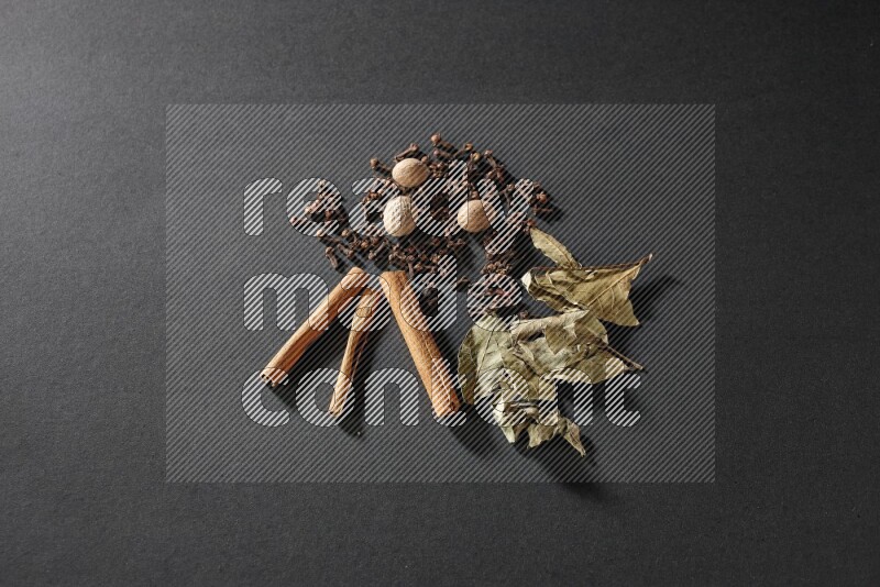 Cloves, ginger, bay laurel and cinnamon sticks on black flooring