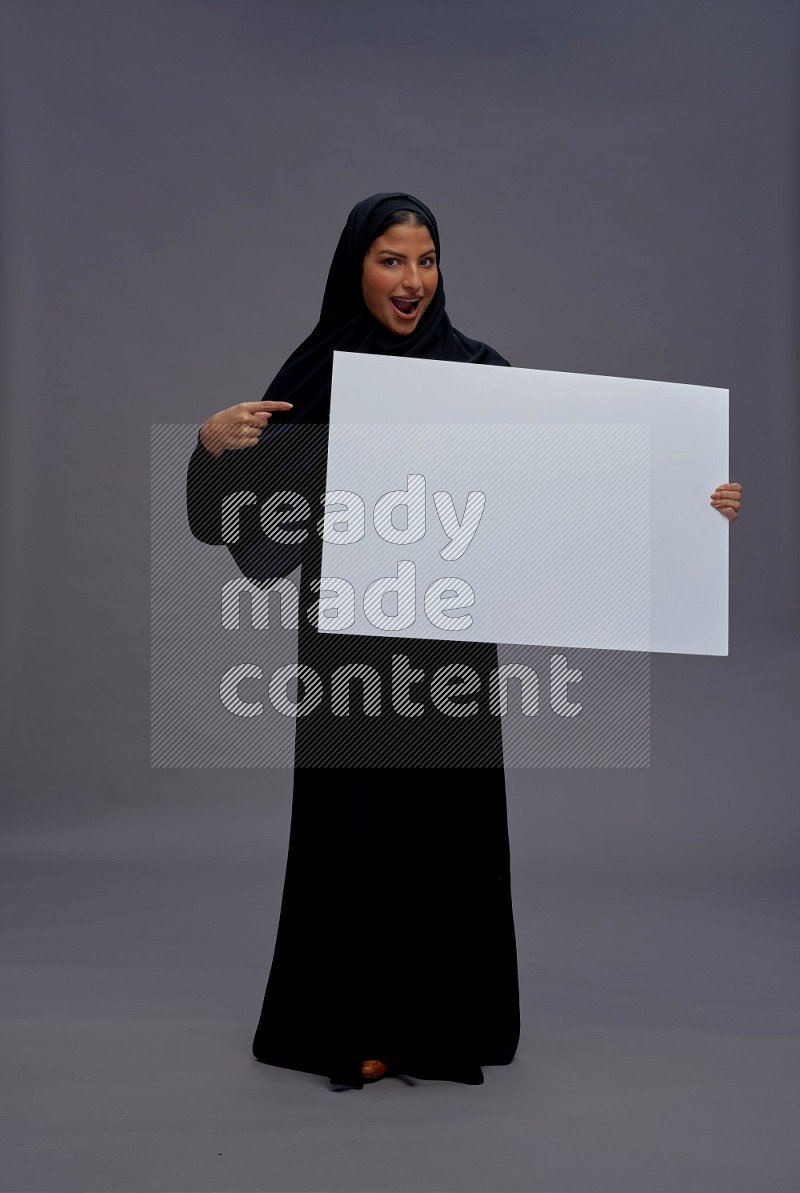 Saudi woman wearing Abaya standing holding white board on gray background