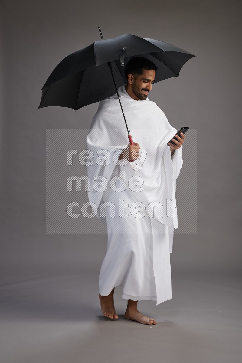 A man wearing Ehram Standing holding umbrella on gray background