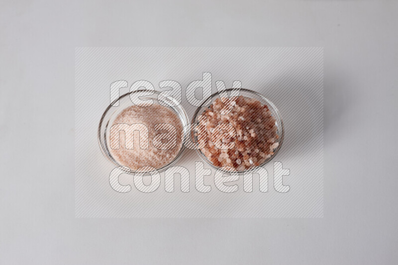 2 glass bowls one is filled with fine himalayan salt and the other with coarse himalayan salt on white background
