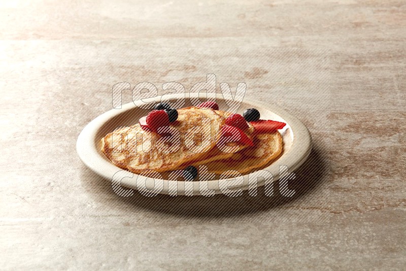 Three stacked mixed berries pancakes in a beige plate on beige background