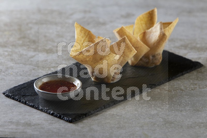 wonton cups with soy sauce ramkin on rectangle slate on grey textured counter top