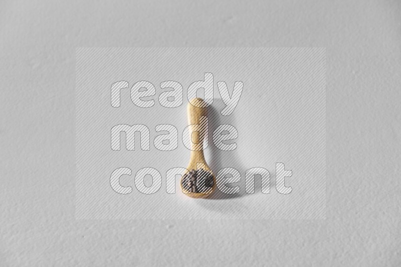 حبوب الفلفل الأسود في ملعقة خشبية علي خلفية بيضاء