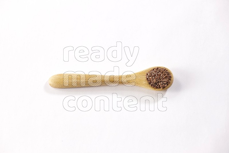 A wooden spoon full of flax seeds on a white flooring