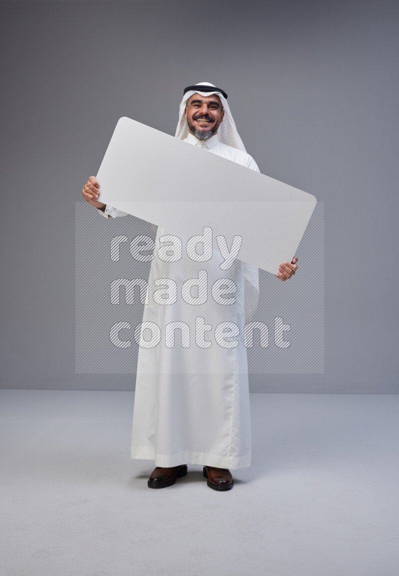 Saudi man Wearing Thob and white Shomag standing holding board on Gray background