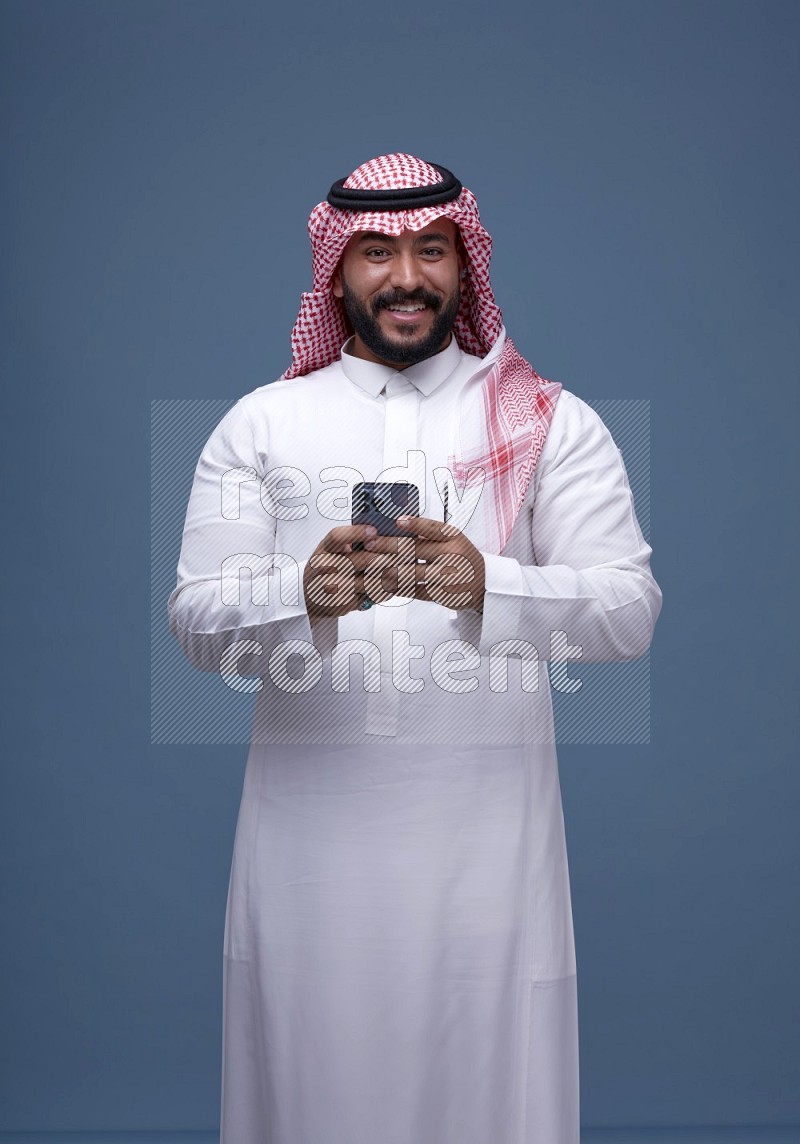 A man Texting on Blue Background wearing Saudi Thob and Shomag