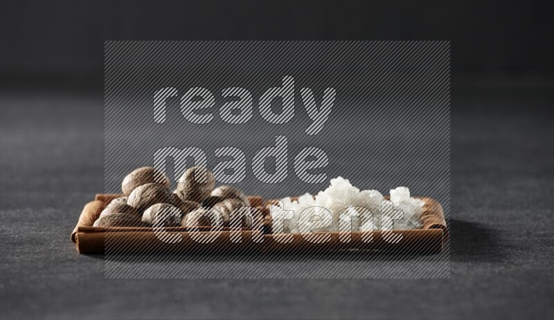 مربعان من أعواد القرفة ممتلئان بجوزة الطيب والملح الأبيض علي خلفية سوداء