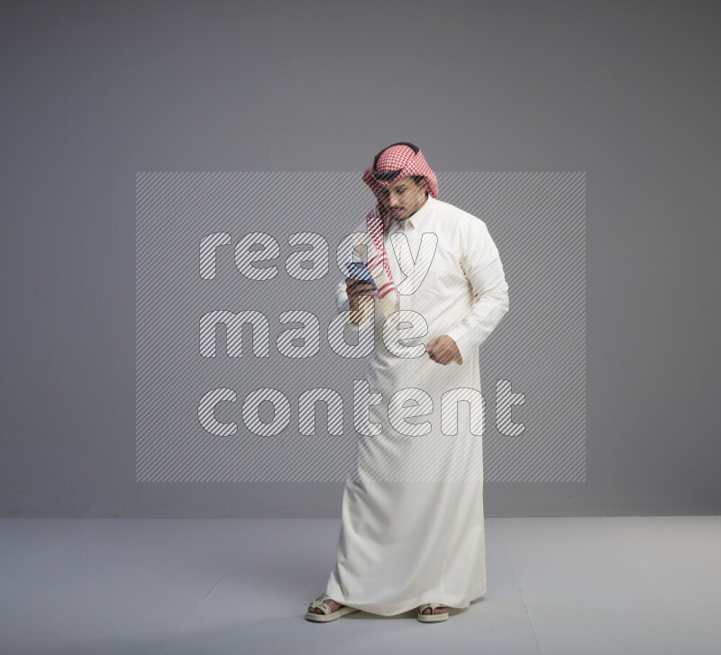 رجل سعودي يرتدي ثوب ابيض وشماغ احمر يمسك جواله بيده