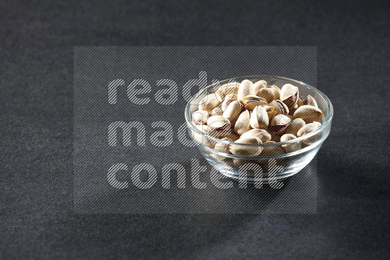 A glass bowl full of pistachios on a black background in different angles