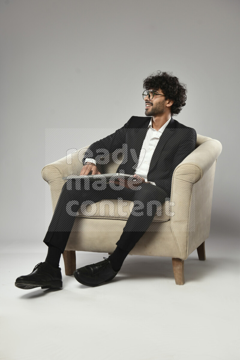 A man wearing formal sitting on a chair holding a laptop on white background