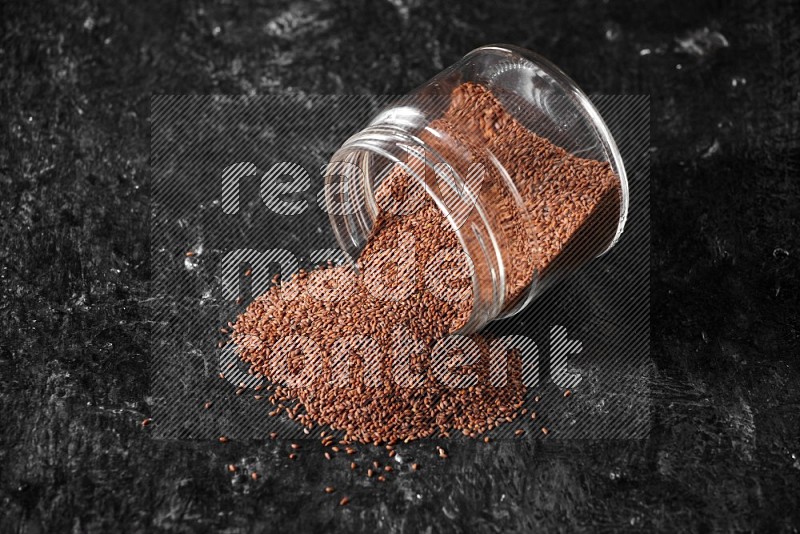 A glass jar full of garden cress seeds flipped and seeds spread out on a textured black flooring
