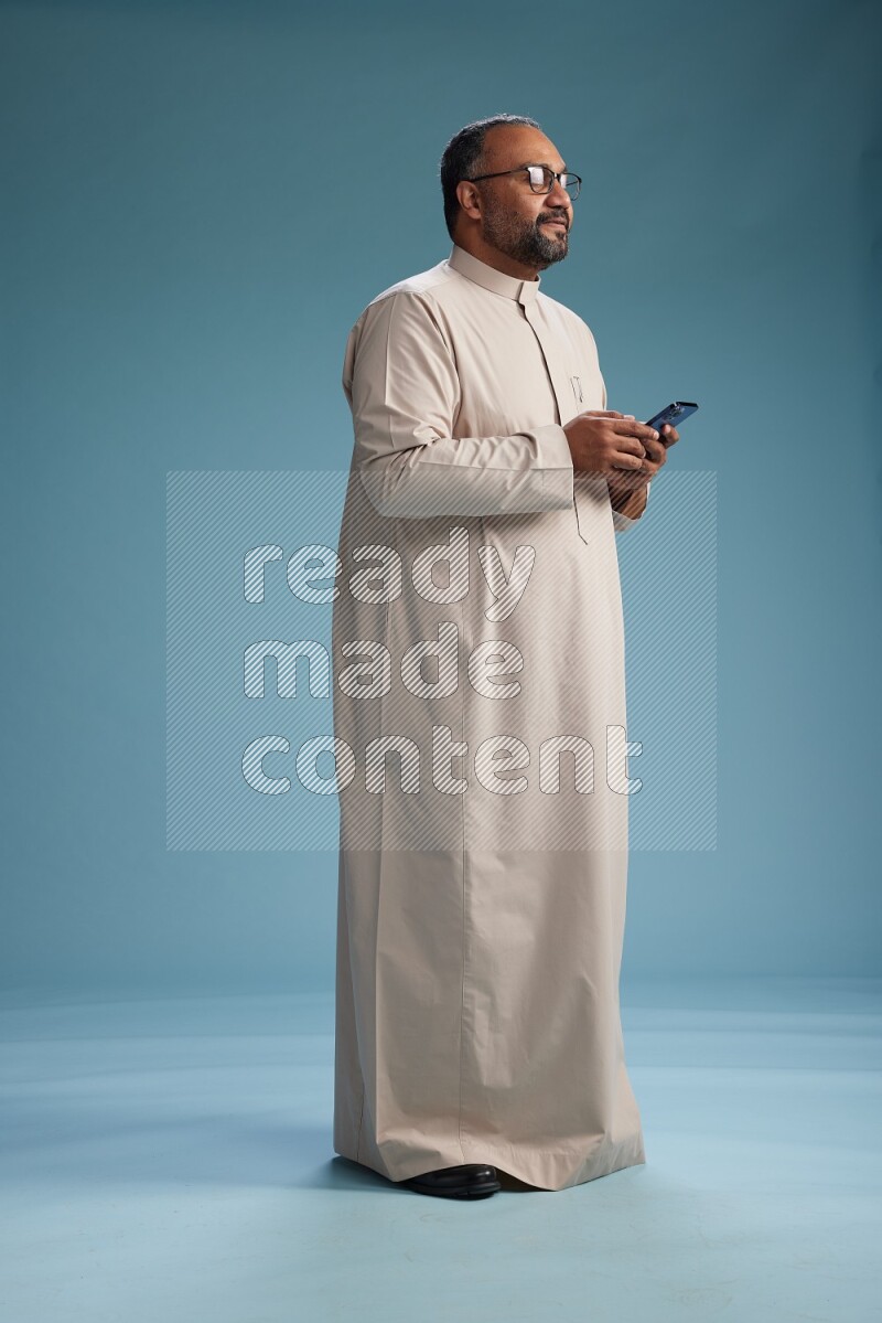 Saudi Man without shimag Standing texting on phone on blue background