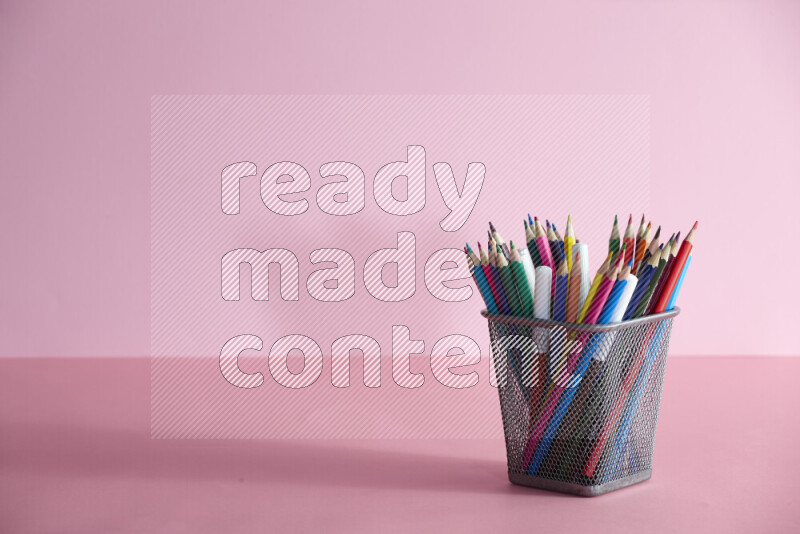 Pens, pencils and other different school supplies in a metal pen holder on rose background