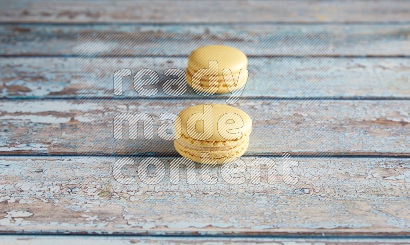 45º Shot of two Yellow Vanilla macarons on a light blue wooden background
