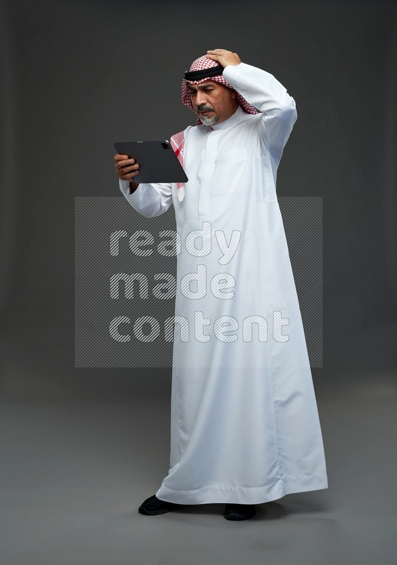 Saudi man with shomag Standing working on tablet on gray background