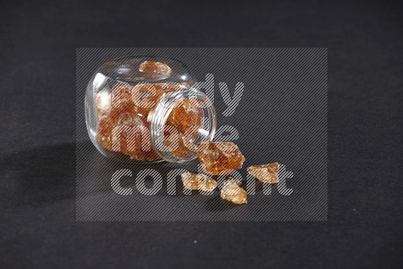 A glass spice jar full of gum arabic and jar is flipped with fallen gum on black flooring in different angles