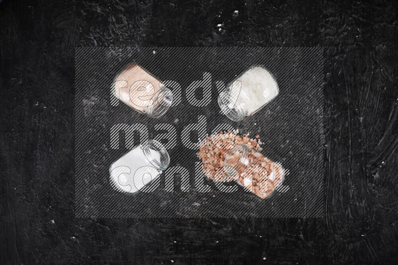 4 glass jars filled with table salt, coarse sea salt, fine himalayan salt and coarse himalayan salt on black background