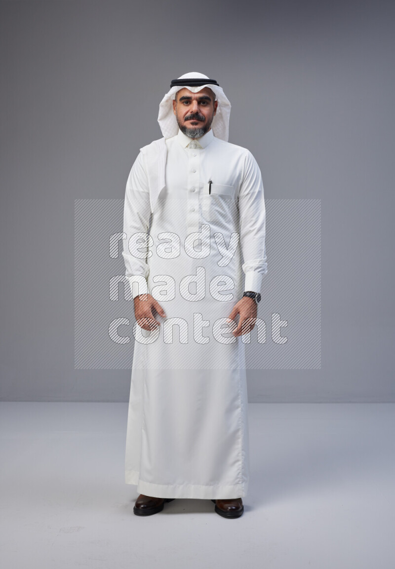 Saudi man Wearing Thob and white Shomag standing interacting with the camera on Gray background