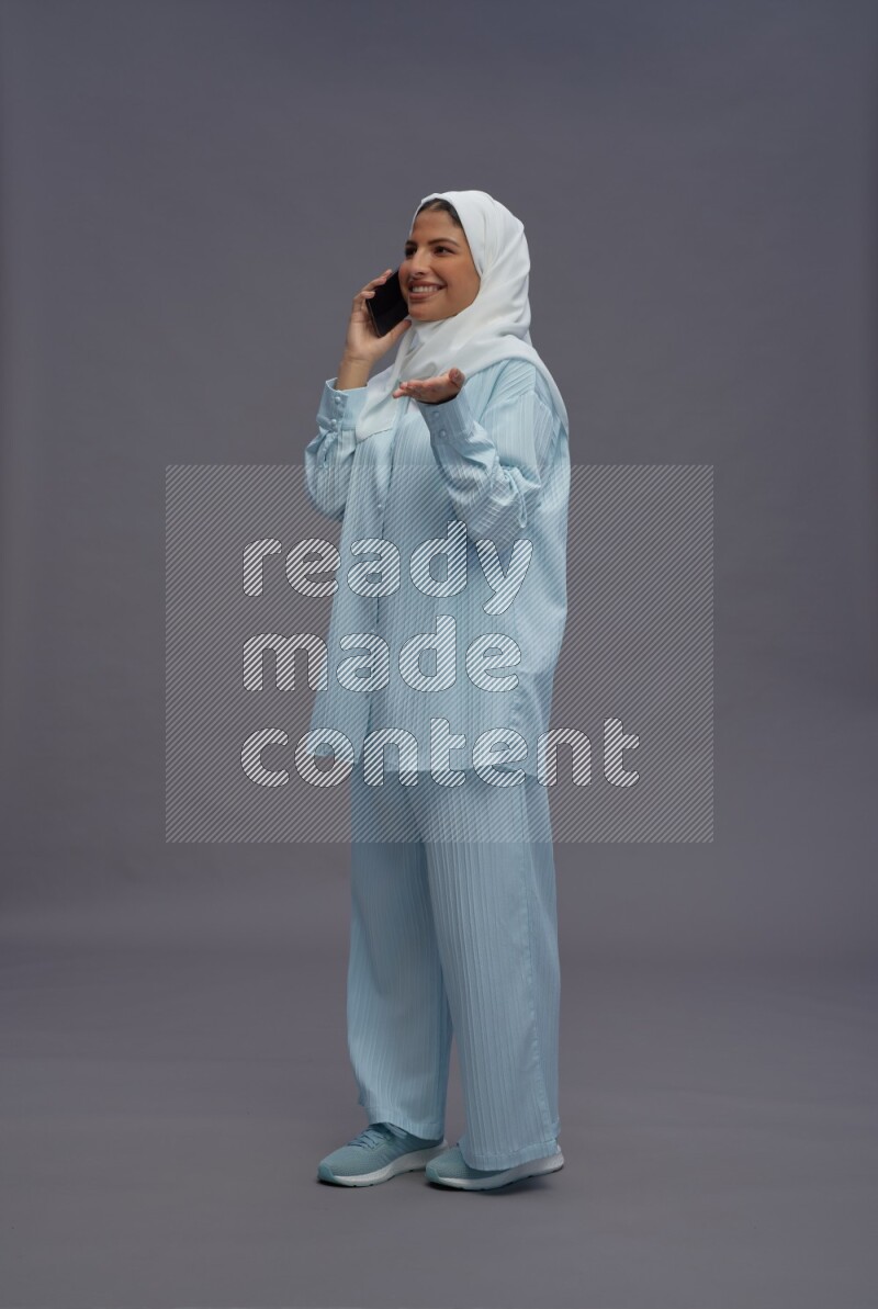 Saudi woman wearing hijab clothes standing talking on phone on gray background