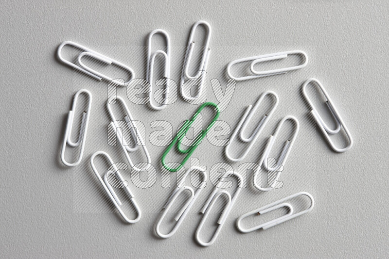 A bunch of white paper clips with a different colored paper clip in the center on grey background