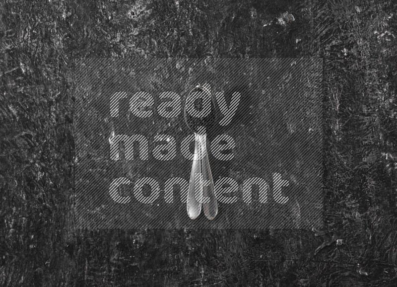 2 metal spoons full of black seeds on a textured black flooring