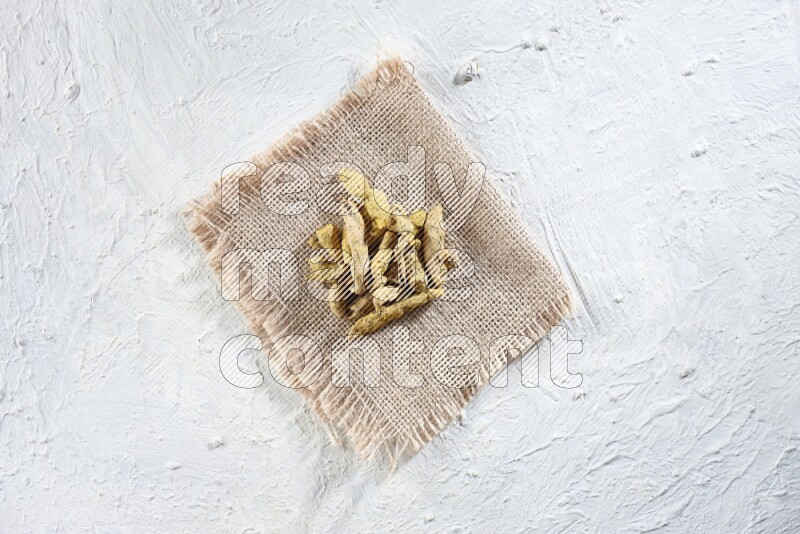 Dried turmeric whole fingers on a piece of burlap on a textured while flooring
