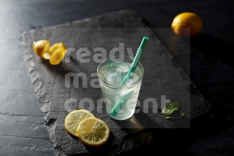 A glass of lemon juice with a straw on black background