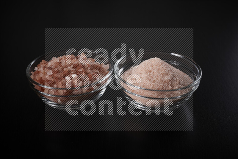 2 glass bowls one is filled with fine himalayan salt and the other with coarse himalayan salt on black background