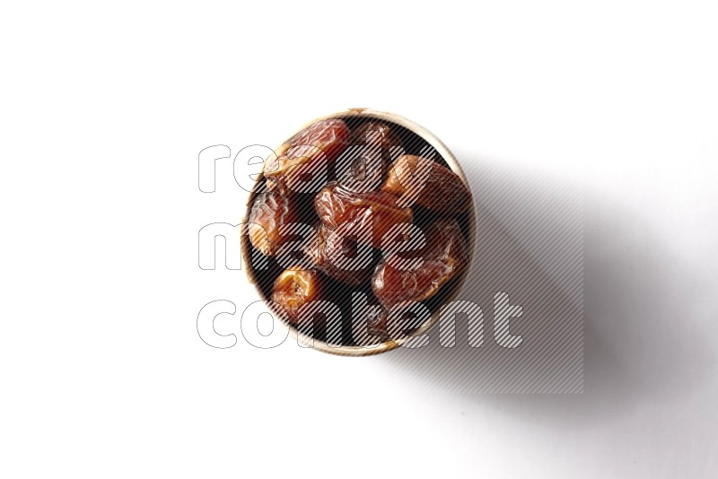 Dates in a beige pottery bowl on white background