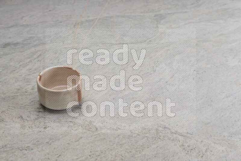 A small beige pottery bowl on grey marble background