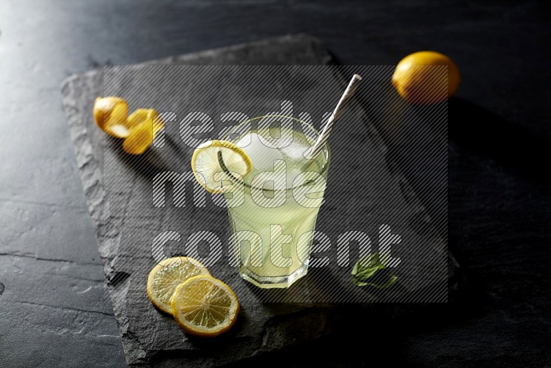 A glass of lemon juice with a straw on black background