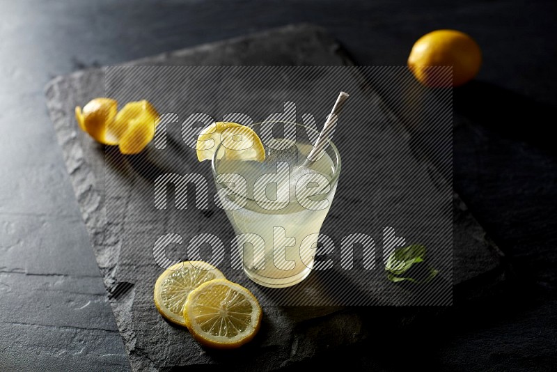 A glass of lemon juice with a straw on black background