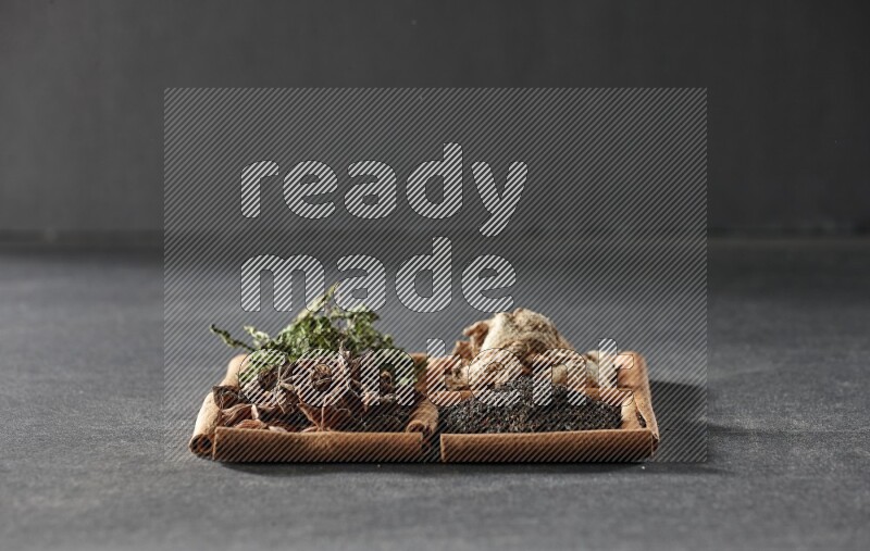 4 squares of cinnamon sticks full of black tea, dried ginger, dried mint leaves and star anise on black flooring