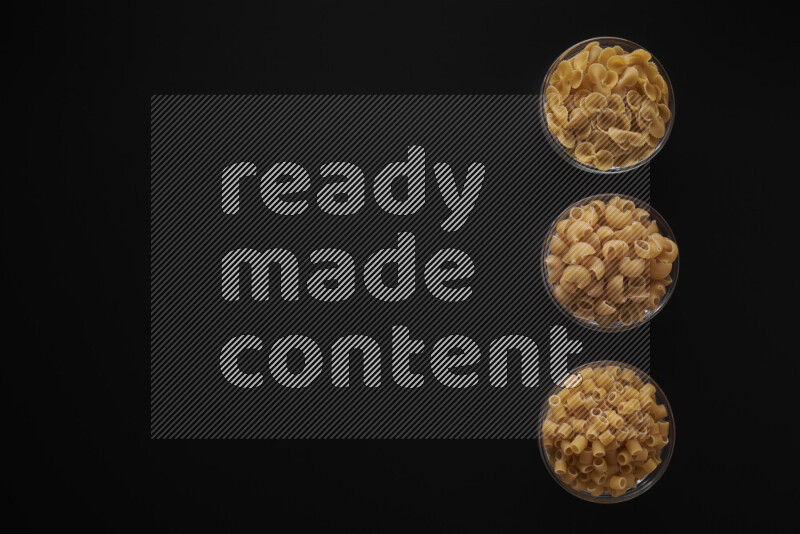 Different pasta types in 3 glass bowls on black background