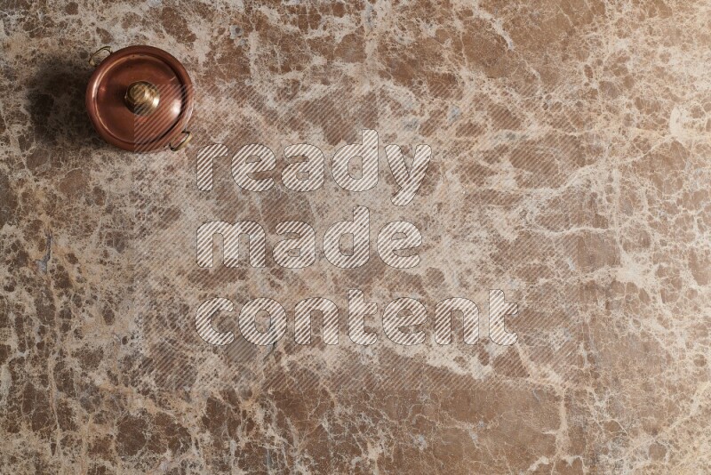 A small copper pot on beige marble background