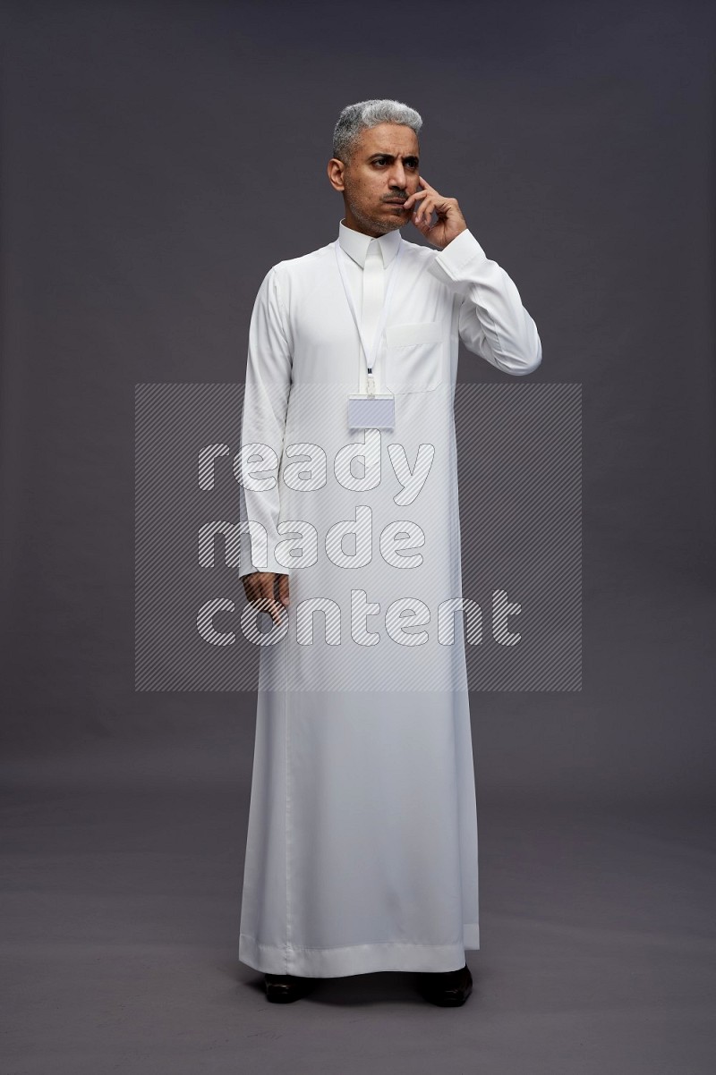 Saudi man wearing thob with neck strap employee badge standing interacting with the camera on gray background