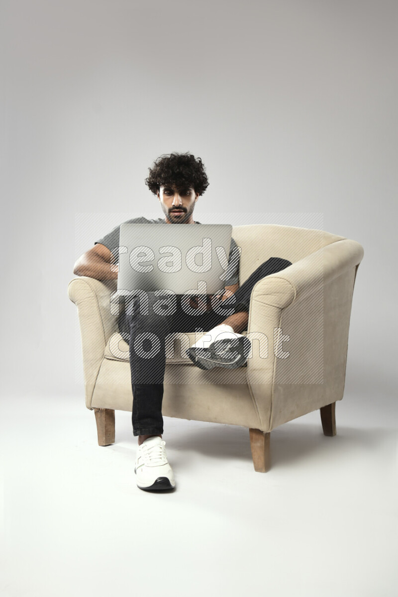A man wearing casual sitting on a chair working on a laptop on white background
