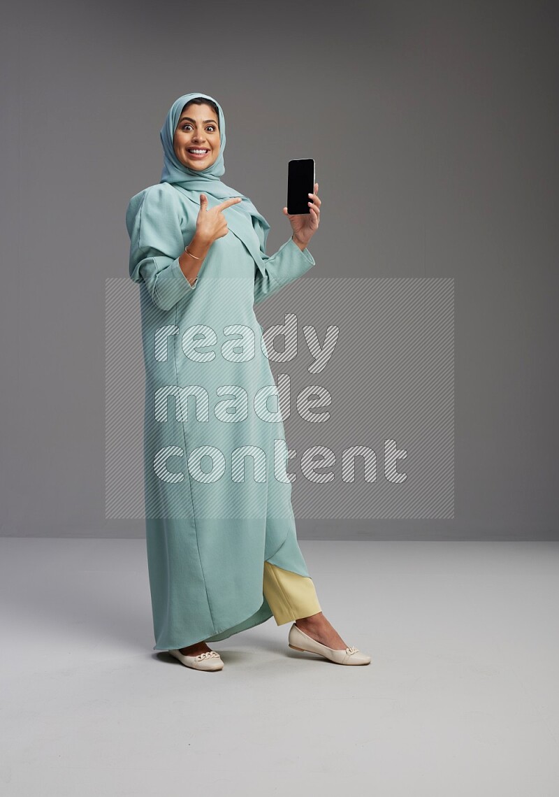 Saudi Woman wearing Abaya standing showing phone to camera on Gray background