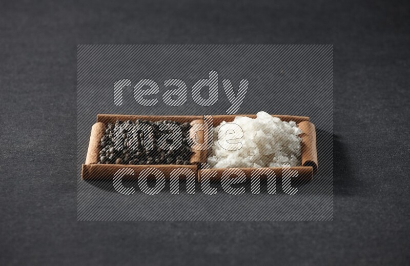 مربعان من أعواد القرفة ممتلئان بالملح الأبيض وحبوب الفلفل الأسود علي خلفية سوداء