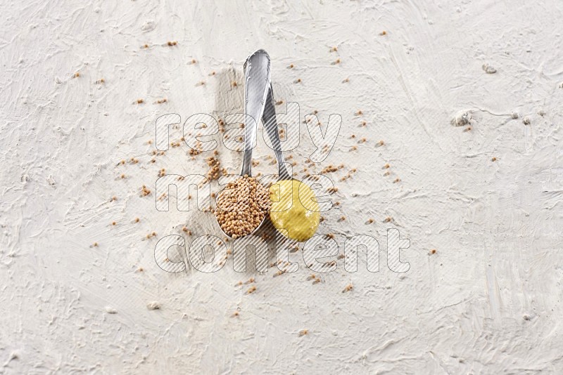 2 metal spoons filled with mustard seeds and mustard paste on a textured white flooring in different angles