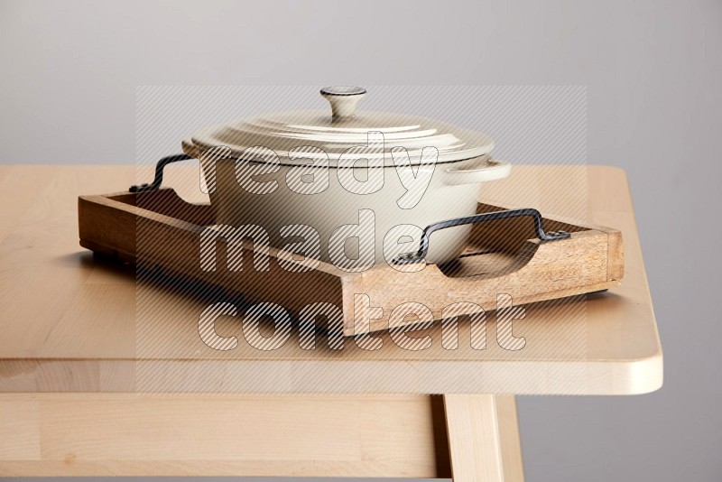 white ceramic pot on a rectangular wooden tray with handles on the edge of wooden table