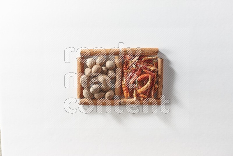 مربعان من أعواد القرفة ممتلئان بالفلفل الحار المجفف وجوزة الطيب علي خلفية بيضاء