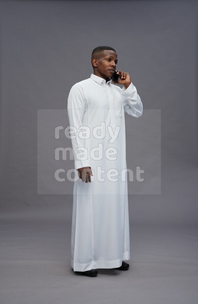 Saudi man wearing thob standing talking on phone on gray background