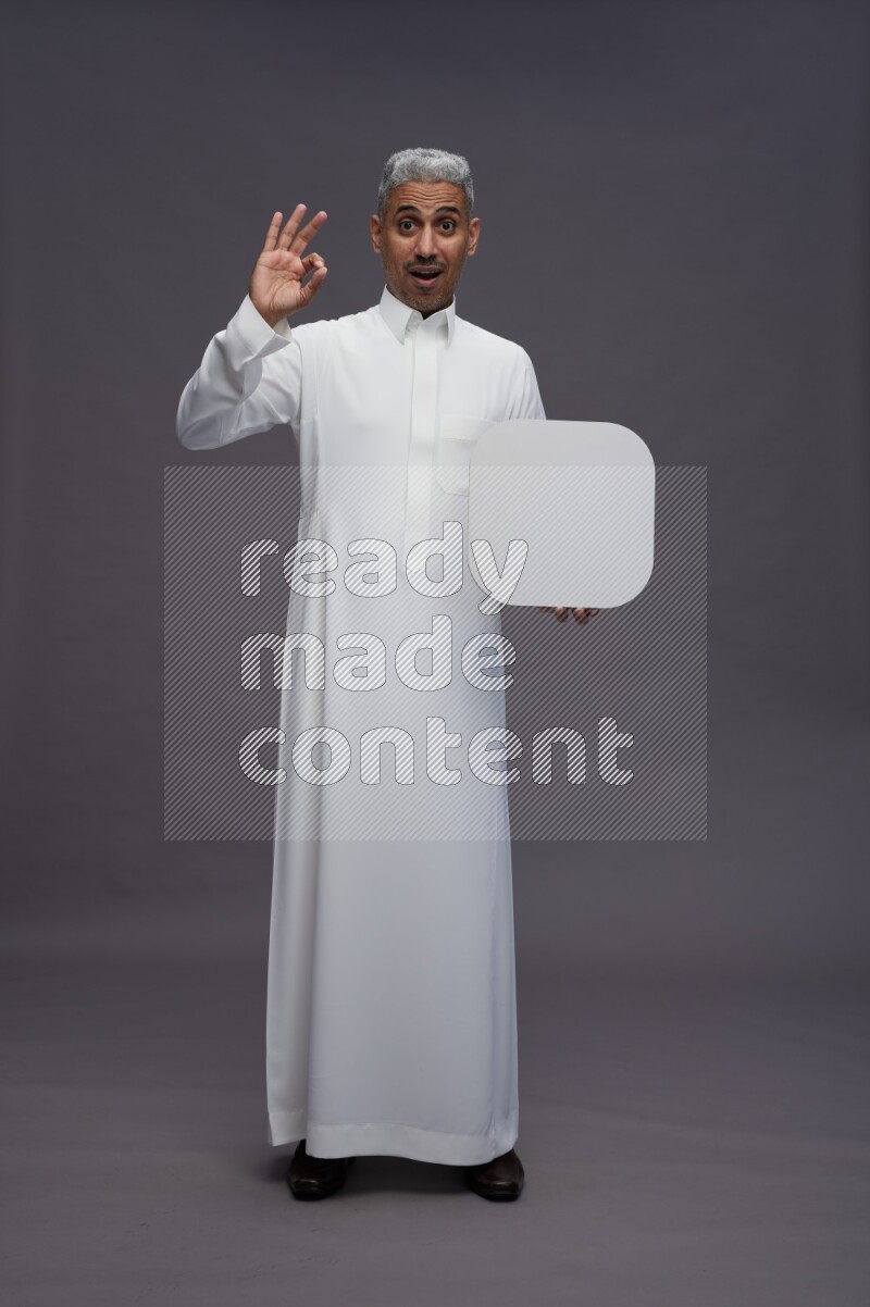 Saudi man wearing thob standing holding social media sign on gray background