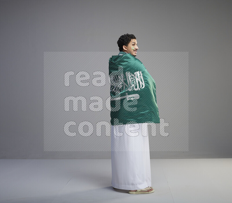 رجل سعودي يرتدي ثوب ابيض يلف علم السعودية حوله